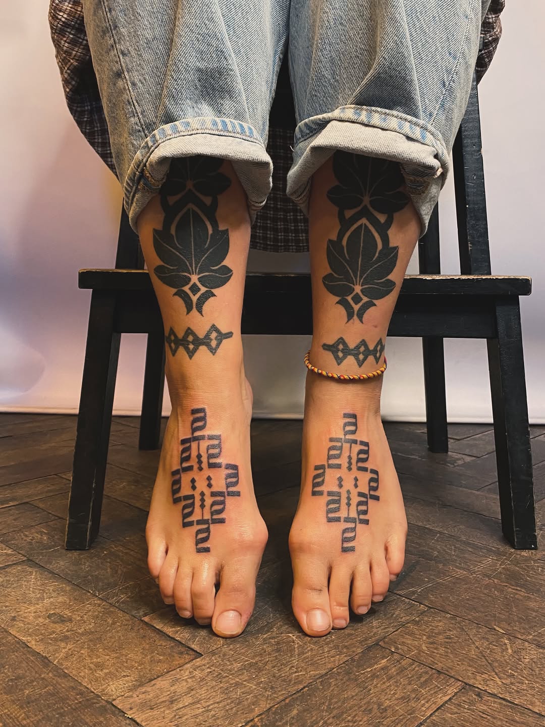 Symmetrical geometric and ornamental tattoos on both calves and feet, featuring leafy mandalas and repeating linear patterns.