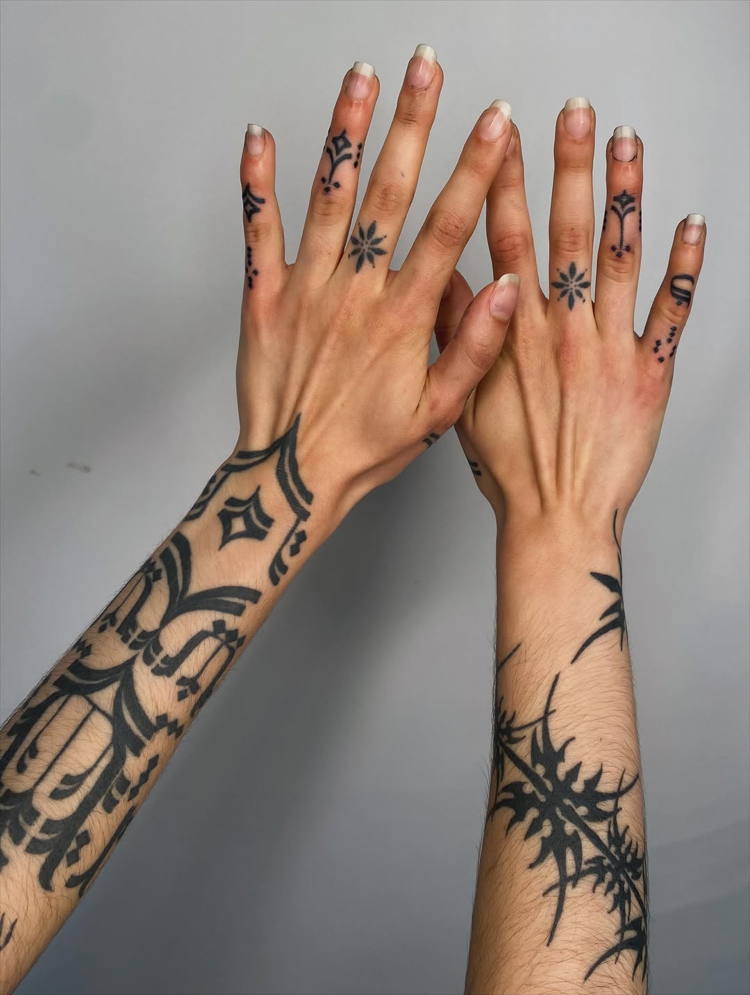 Hands displaying geometric and ornamental black tattoos on fingers, forearms, and wrists with symmetrical patterns and dotwork elements.