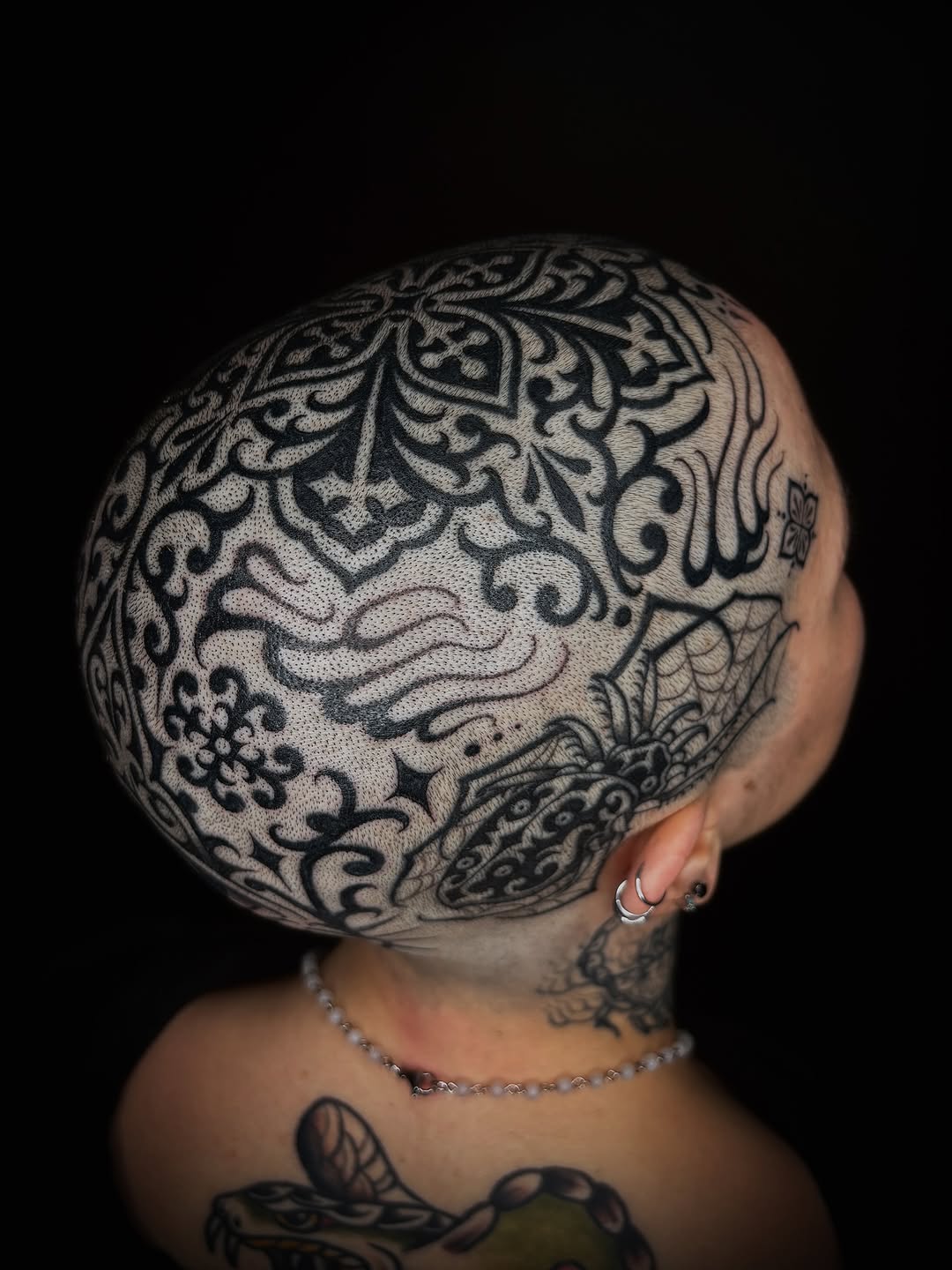 Ornate black mandala and baroque scrollwork tattoo covering the entire head in symmetrical ornamental patterns.