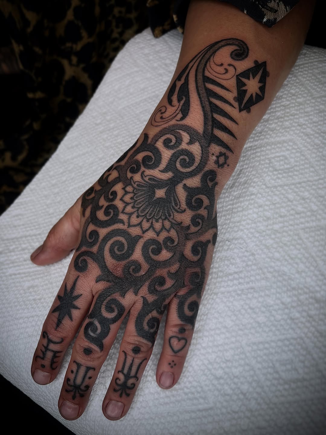 Ornamental black geometric and scrollwork tattoo covering the hand and forearm with symmetrical spiral motifs and decorative flourishes.