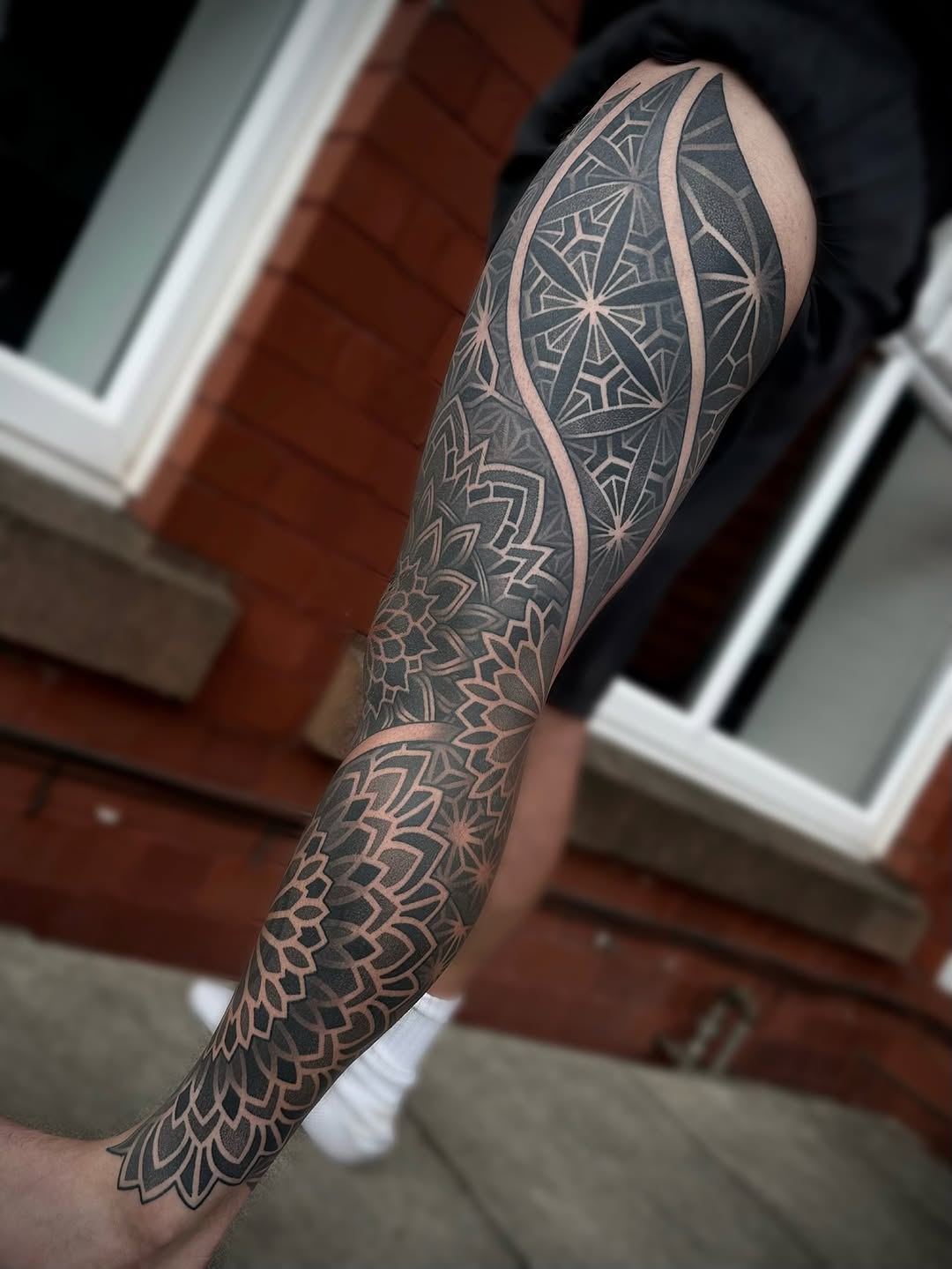 Full sleeve geometric mandala and star pattern tattoo with curved dividing lines in black and grey on forearm and upper arm.