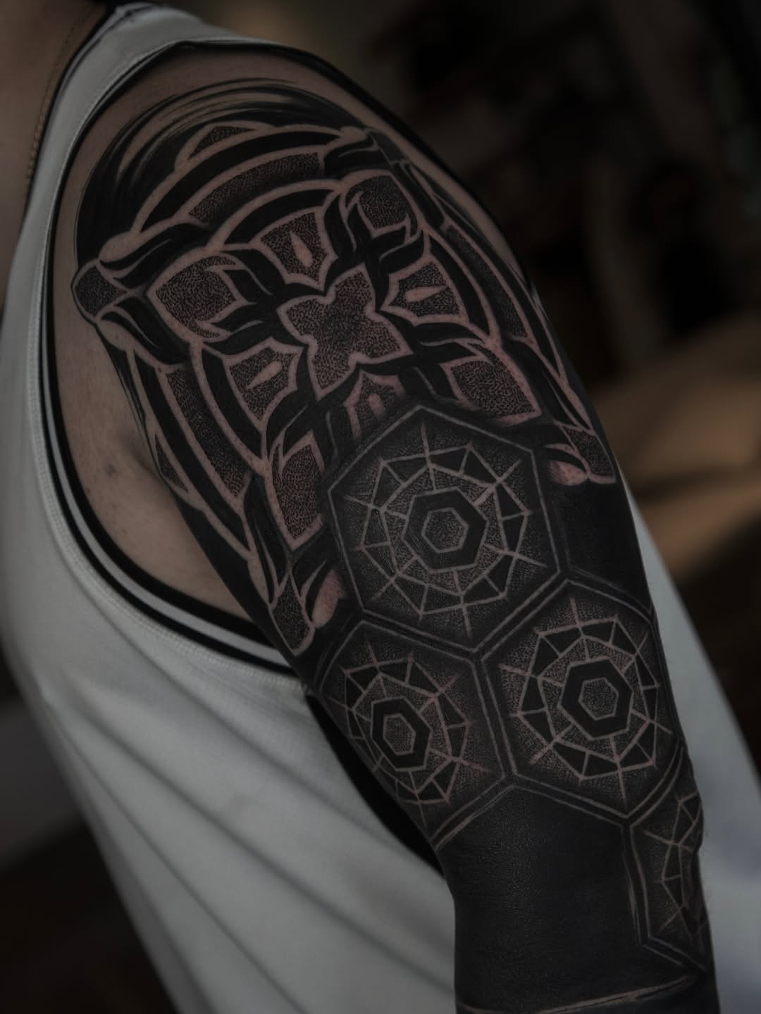 Geometric mandala and ornamental dotwork tattoo covering the shoulder and upper arm with symmetrical stippled patterns.