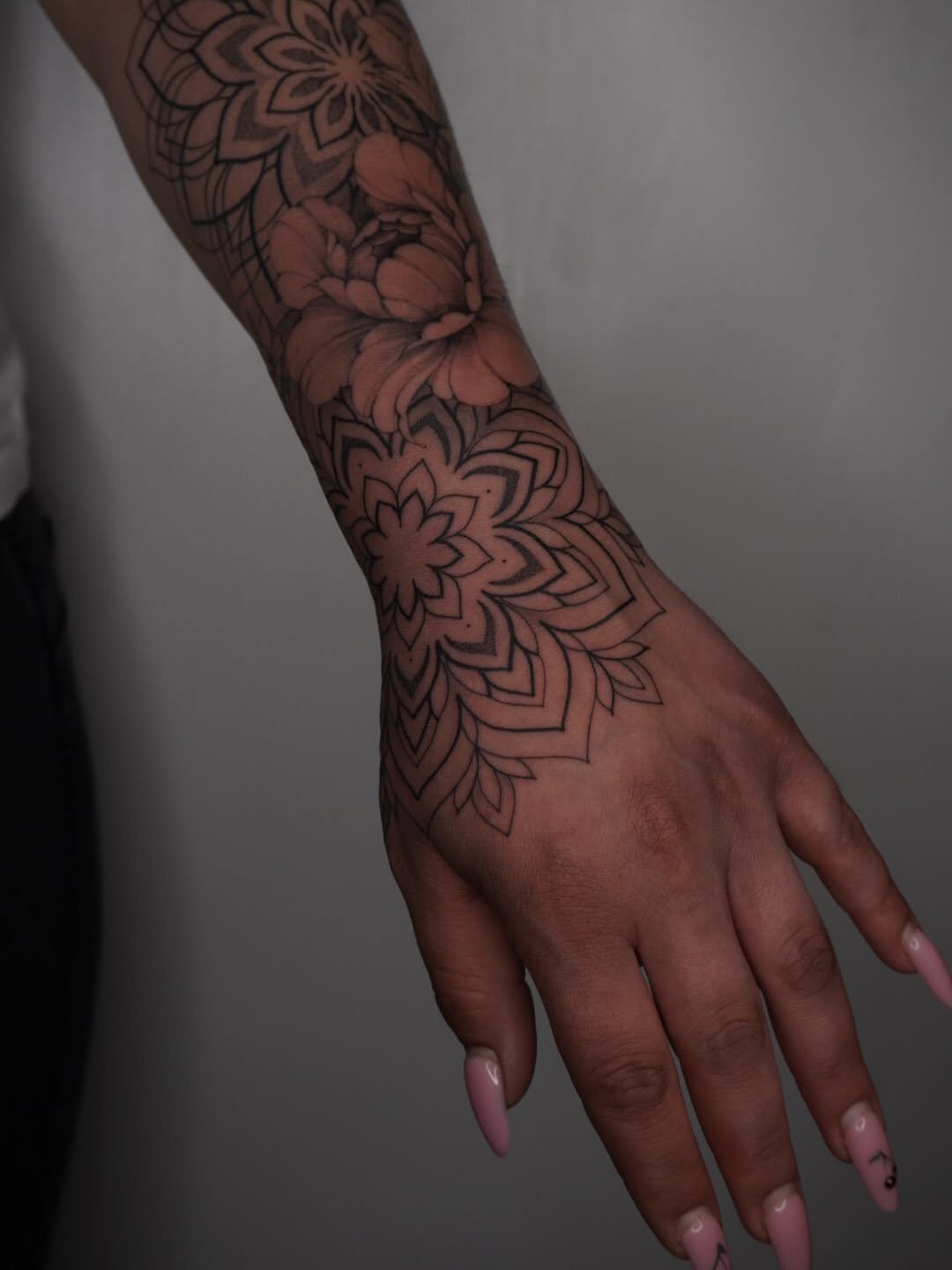 Mandala and floral geometric tattoo sleeve with symmetrical line work covering forearm and hand.
