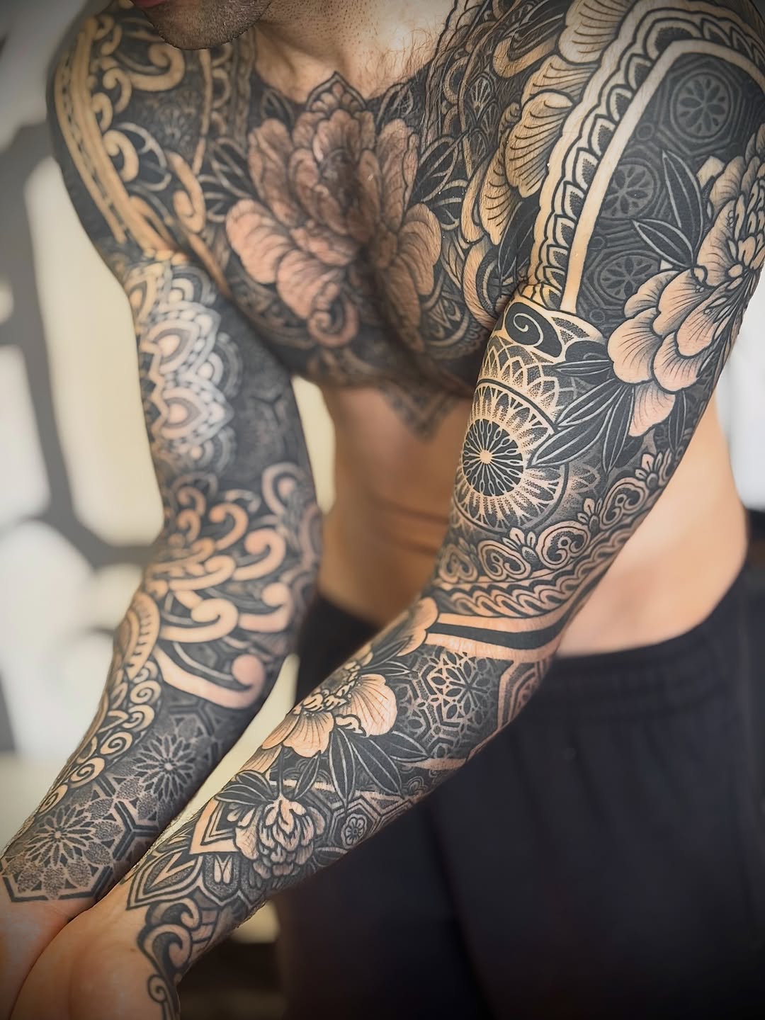 Full sleeve tattoo with ornamental mandalas, floral motifs, and symmetrical geometric patterns in black and gold.