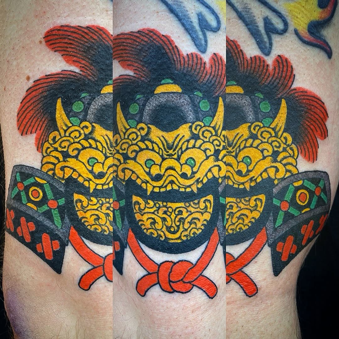 Ornate oni demon mask with red hair, golden scaled armor, decorative chest plate, and red ribbon bow on upper arm.