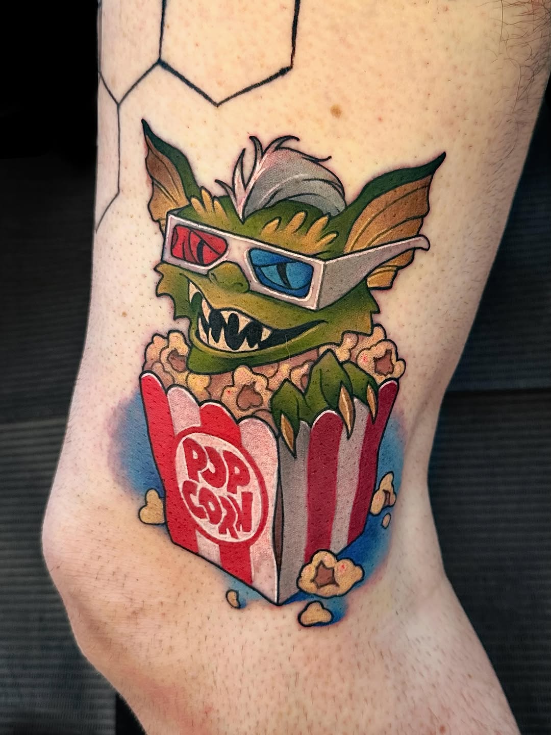 A monstrous creature with sharp teeth wearing 3D glasses emerging from a popcorn box on the thigh.